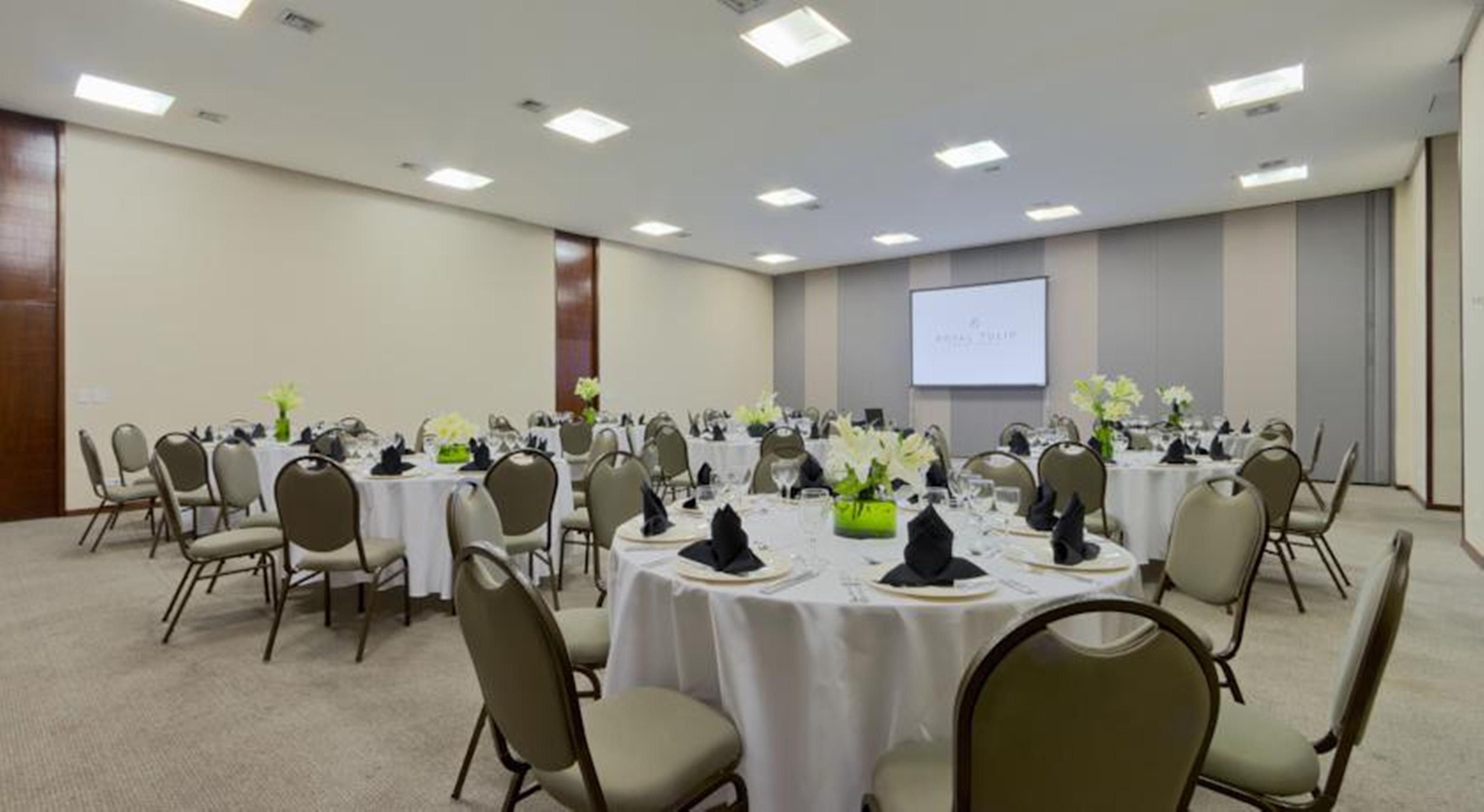 Royal Tulip Brasilia Alvorada Hotel Екстериор снимка The photo shows a banquet or conference room set up with multiple round tables covered in white tablecloths. Each table is arranged with black napkins and centerpieces featuring flowers, likely in shades of green and white. The room has beige walls a